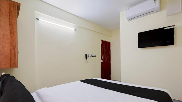 A hotel room with a bed, a wooden wardrobe, a wall-mounted TV, and an air conditioning unit.