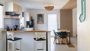A modern kitchen with white cabinetry, a hanging light fixture, and a dining area with a wooden table and chairs. - Townhouse with garage, Saint-Quay-Portrieux (Saint-Quay-Portrieux)