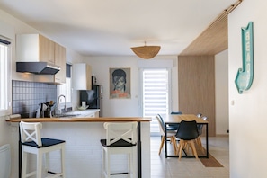 Een moderne keuken met witte kasten, een hanglamp en een eethoek met een houten tafel en stoelen.