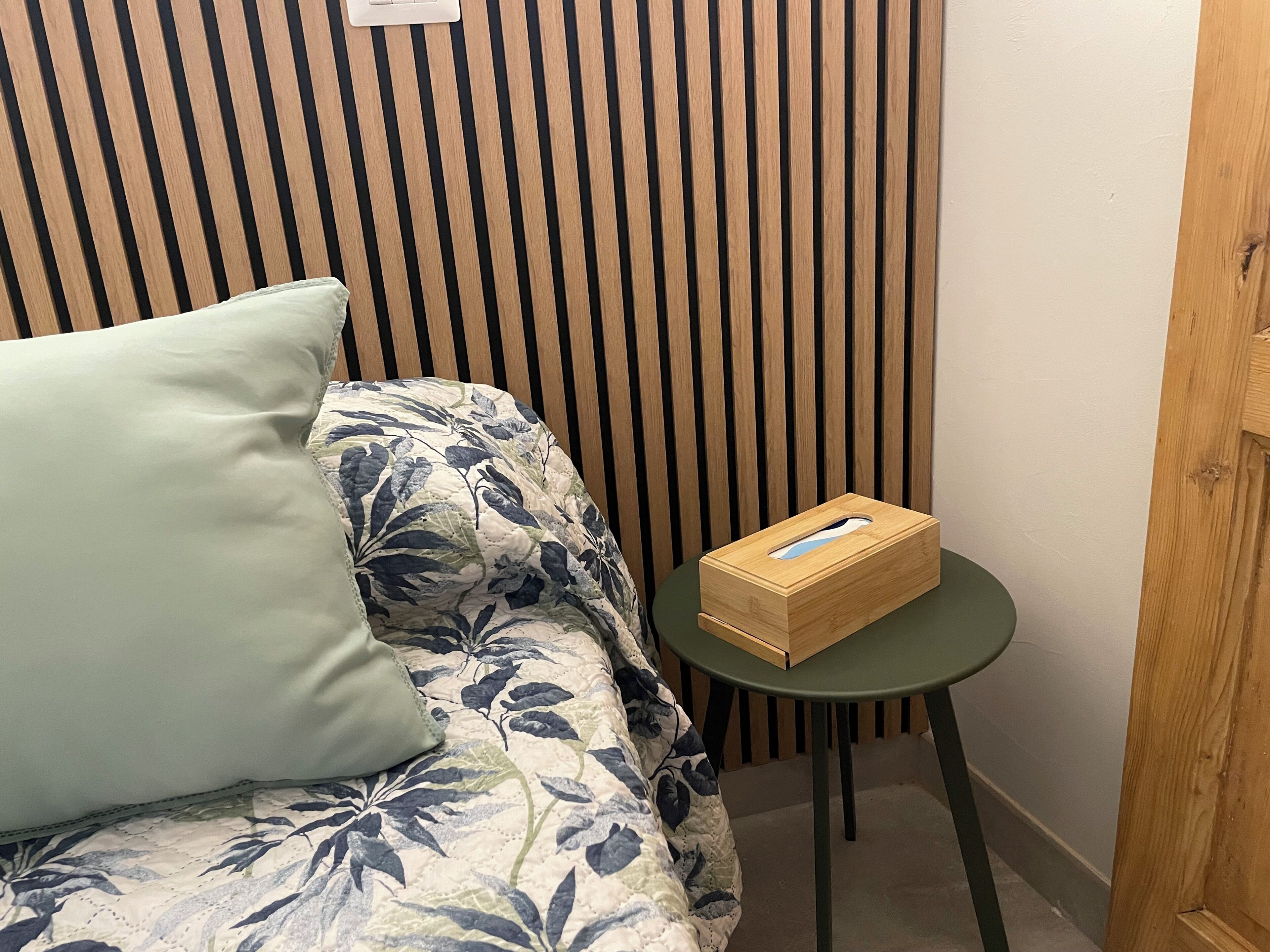 Une pièce avec un mur à rayures, un canapé à motifs floraux, un coussin vert et une petite table ronde sur laquelle se trouve une boîte en bois.
