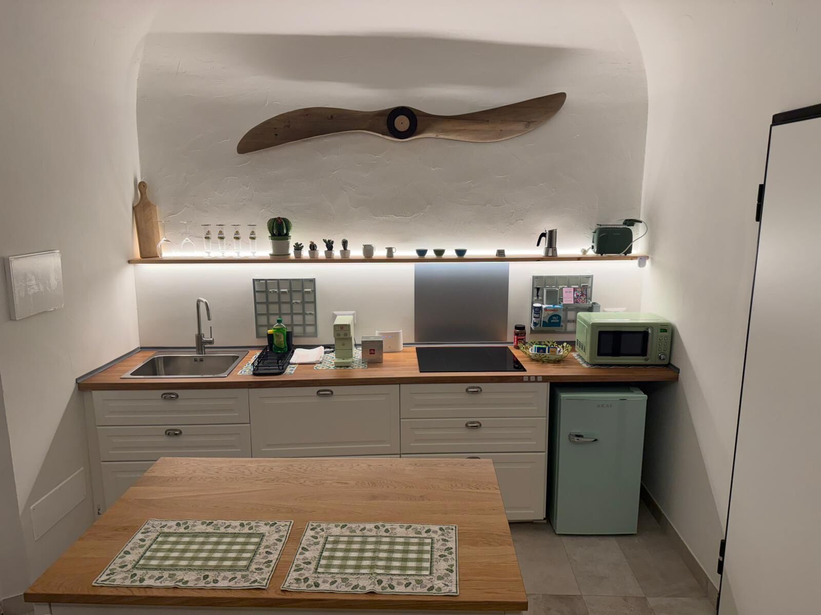 A compact kitchen with a wooden countertop, a built-in microwave, a small refrigerator, and a ceiling fan.