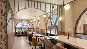 A restaurant with high arched windows, multiple dining tables, and chairs with a variety of patterns. - Hampton By Hilton Madinah Central District (Madinah)