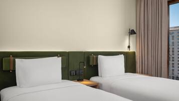 Una habitación de hotel con dos camas, un cabecero verde, una mesita de noche con lámpara y una ventana con cortinas.