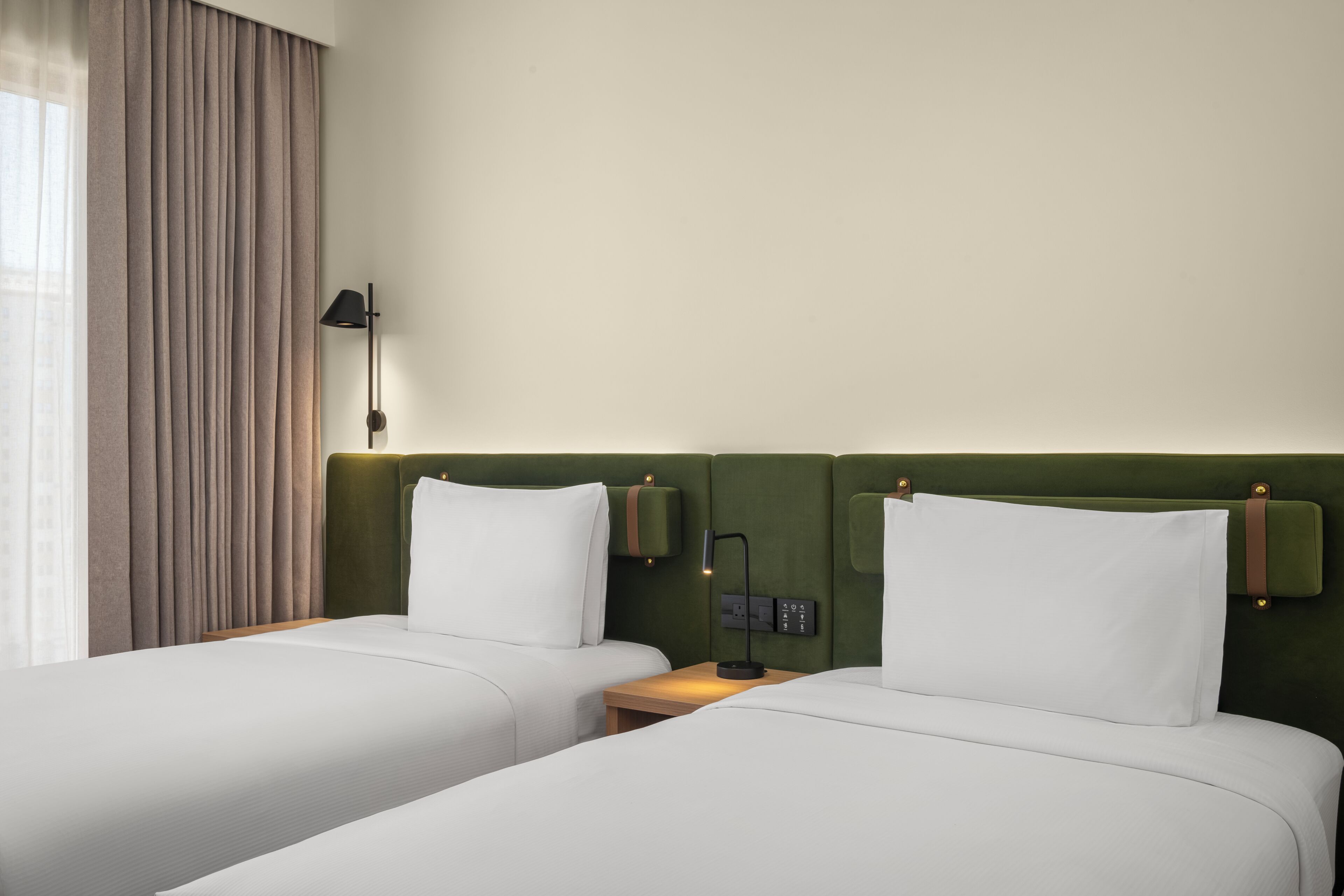 Ein Hotelzimmer mit zwei Betten, einem Nachttisch mit Lampe und einem grünen Kopfteil.