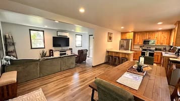 A spacious living area with a wooden dining table, a sofa, and a TV.