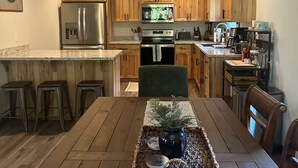 Cozinha moderna com armários de madeira, eletrodomésticos de aço inoxidável e área de refeições com mesa e banquetas de madeira.