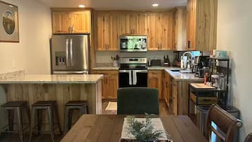 A modern kitchen with wooden cabinets, stainless steel appliances, and a dining area with a wooden table and stools.