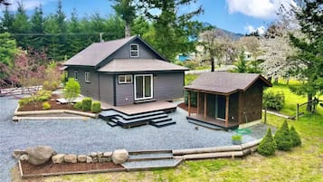 A modern two-story house with a large deck, a small attached cabin, and a well-maintained garden.