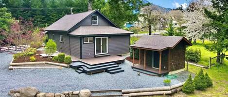 Une maison moderne à deux étages, dotée d’une grande terrasse, d’un petit chalet attenant et d’un jardin bien entretenu.