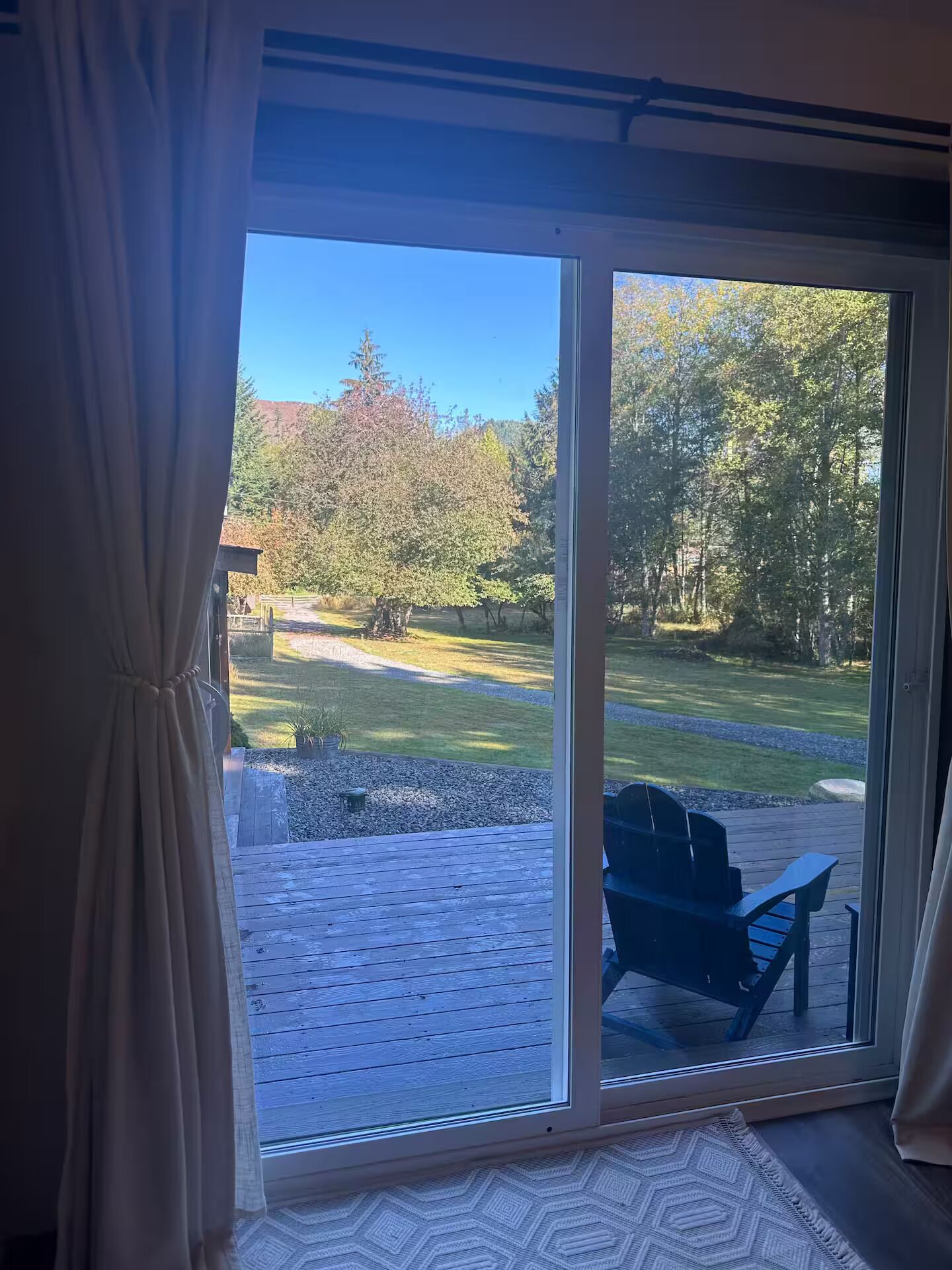 A room with a large sliding glass door leading to an outdoor deck with a wooden floor and a blue chair.
