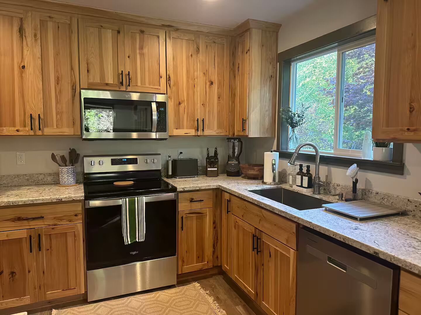 A kitchen with wooden cabinets, stainless steel appliances, a window with a view, and a granite countertop.