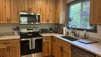 A kitchen with wooden cabinets, stainless steel appliances, a window with a view, and a granite countertop.