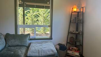 Una habitación con ventana, un sofá, una lámpara y una estantería con objetos.