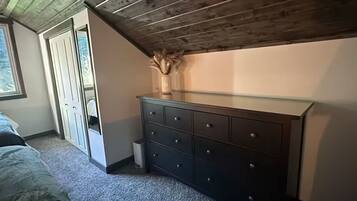 A bedroom with a sloped ceiling, a dresser, a window, and a door.