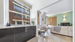 A modern kitchen with a large window, a dining area with a sofa, and a flat-screen TV. - 3 -Berry Street EC1V (London)