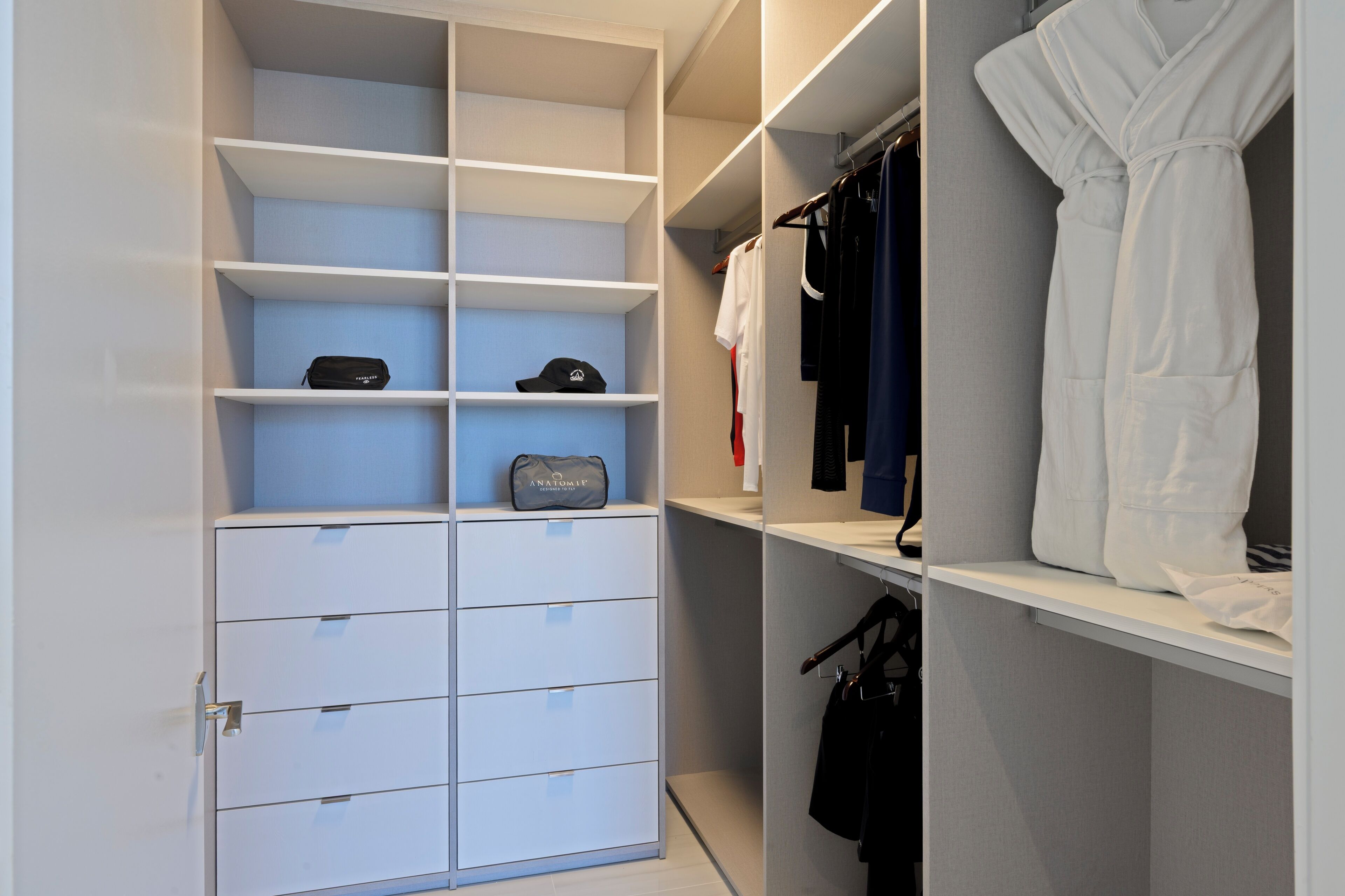 A walk-in closet with multiple shelves and drawers, containing clothing and a bag.