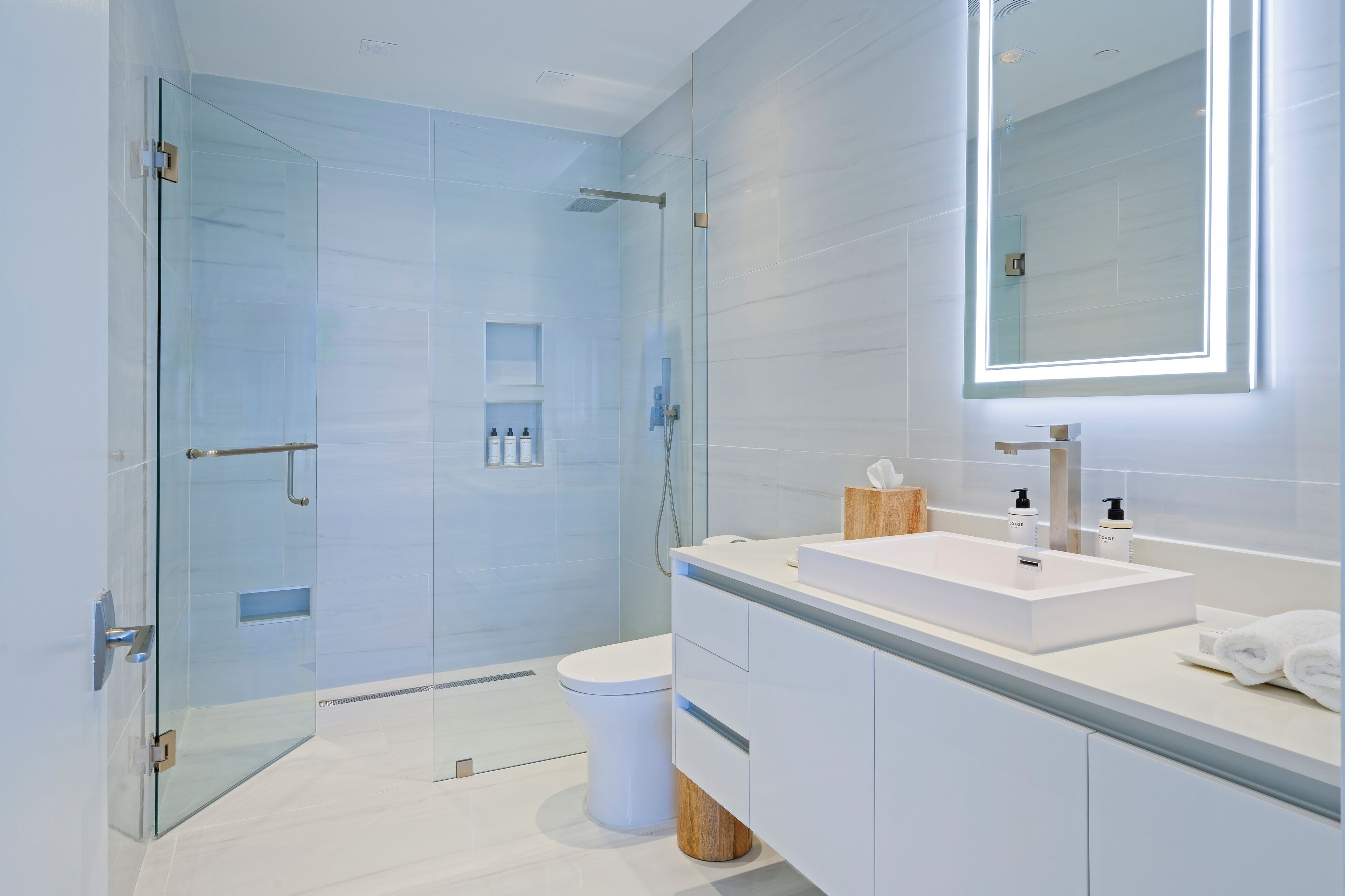 Un baño moderno con cabina de ducha de vidrio, un lavabo blanco y un espejo grande.