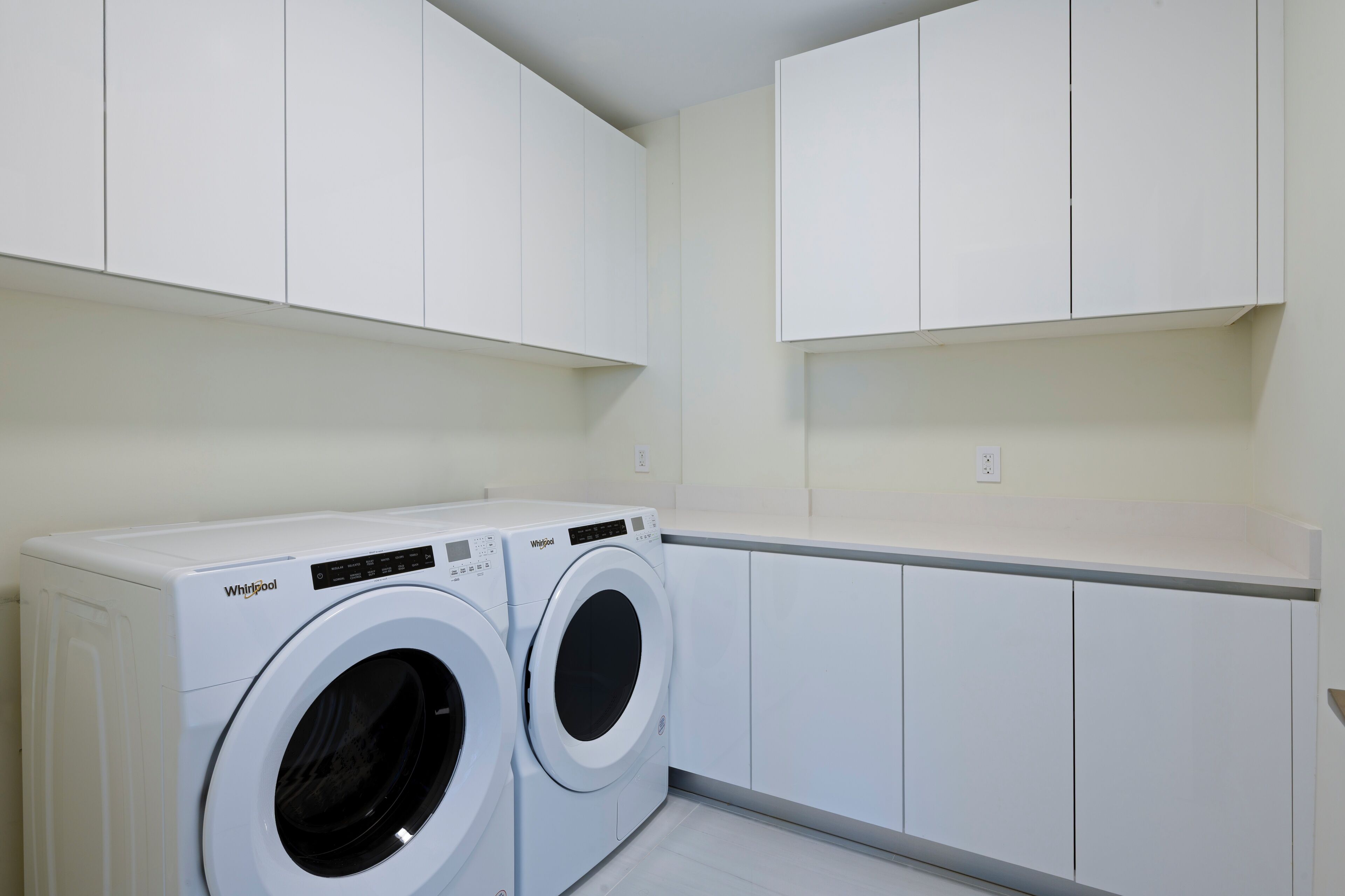 Une buanderie équipée de deux lave-linge Whirlpool blancs, de meubles blancs et d’un plan de travail blanc.