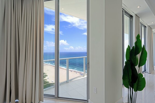 Habitación con una ventana grande que da a una playa, una planta en maceta y una decoración de estilo moderno.