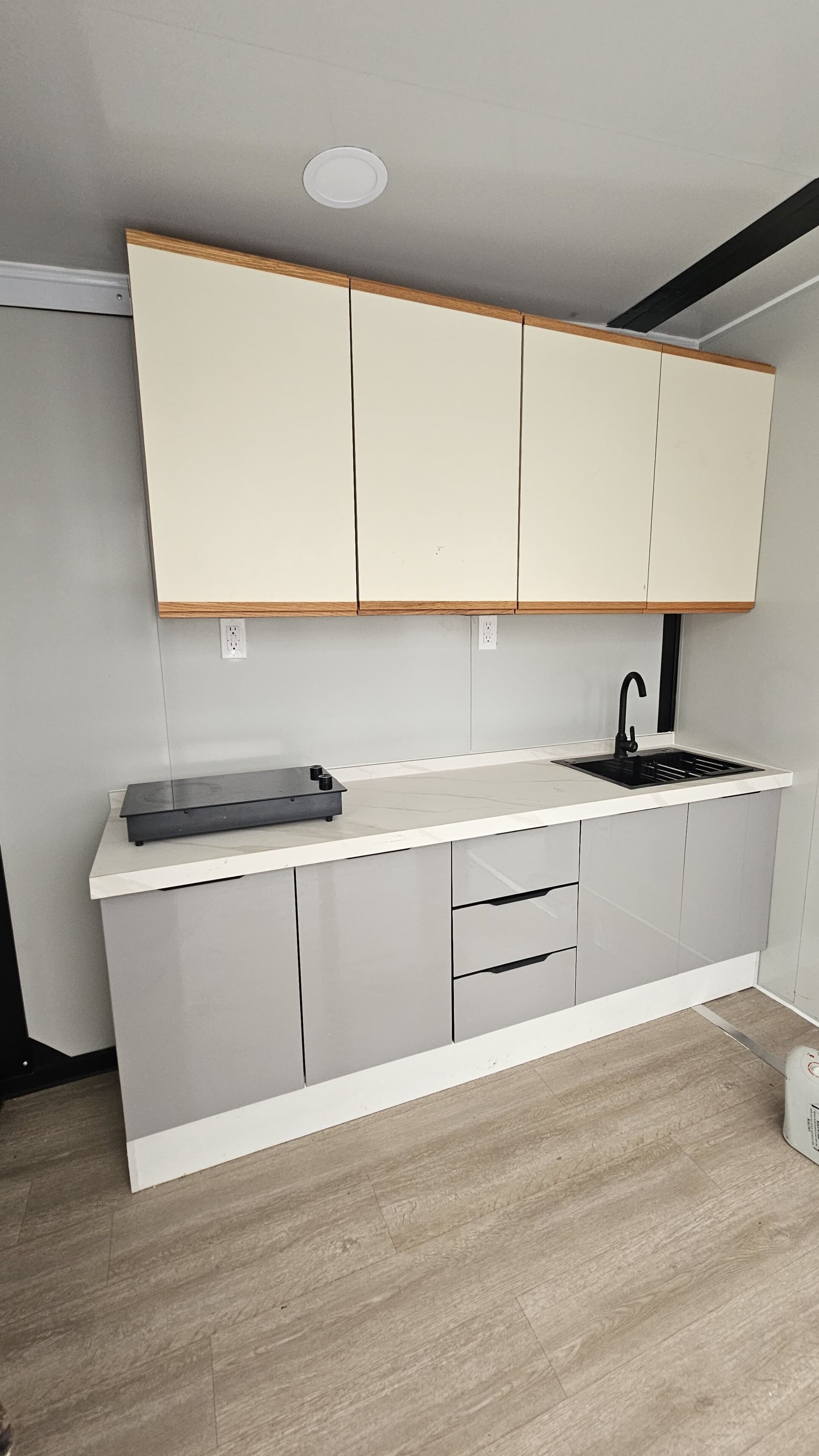 A modern kitchen with a white countertop, black faucet, and grey cabinets.