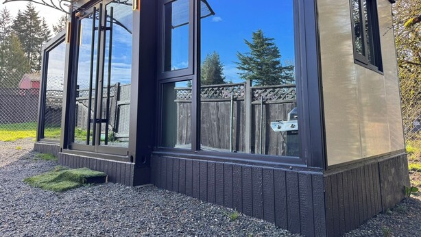 Een modern, compact gebouw met grote ramen, een houten terras en een metalen hek.