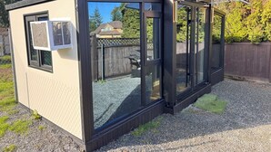 Een klein, afgesloten buitenconstructie met een schuifdeur van glas, een raam met een airconditioning en een metalen dak.