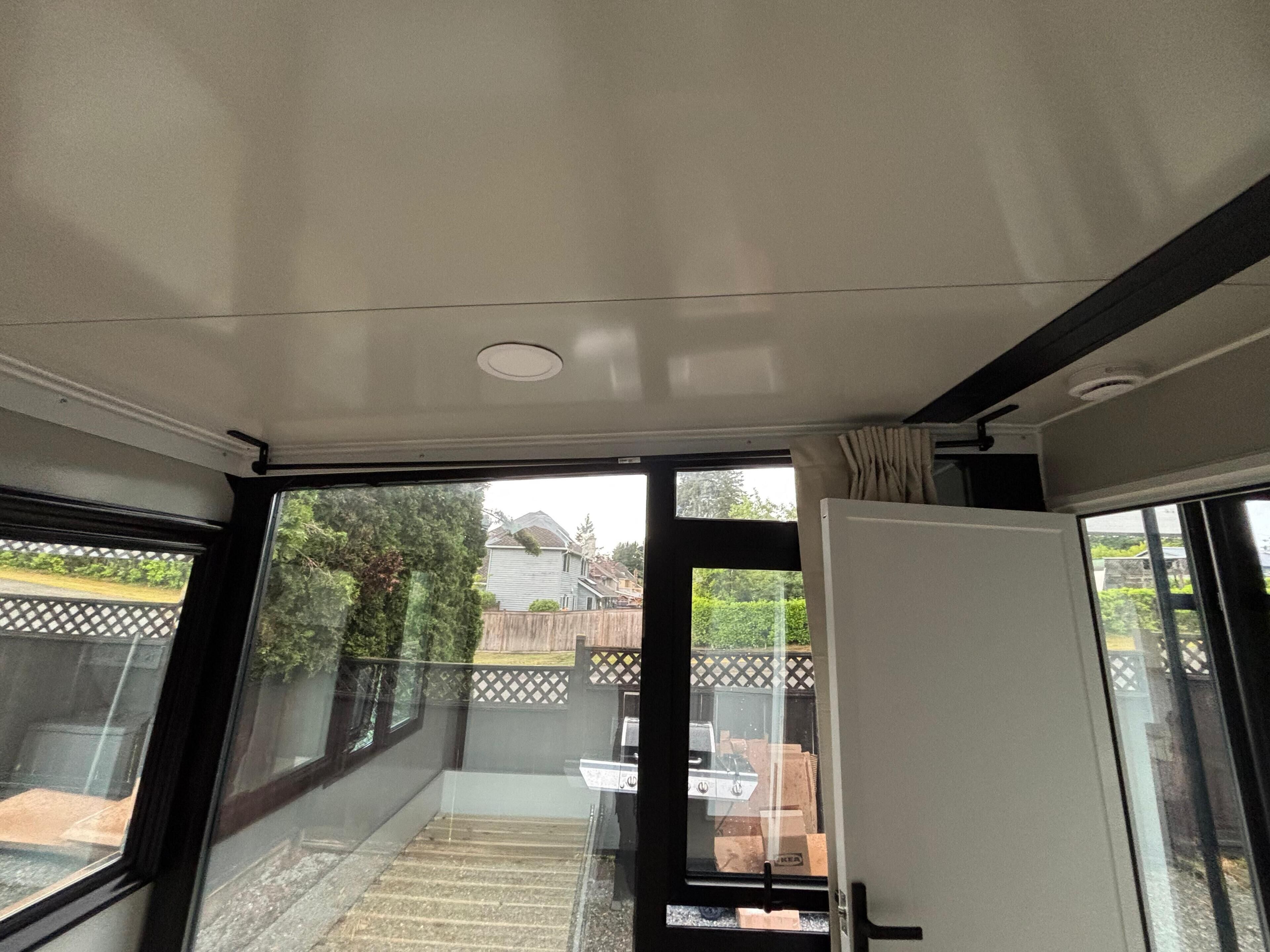 A room with a sliding glass door leading to a balcony, a white ceiling, and a visible outdoor area with a fence and greenery.