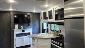 Una cocina moderna con armarios blancos, un refrigerador de acero inoxidable, un horno integrado y un televisor de pantalla plana.