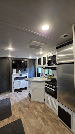 Una cocina moderna con armarios blancos, un refrigerador de acero inoxidable, una estufa a gas y un televisor de pantalla plana montado sobre la encimera.