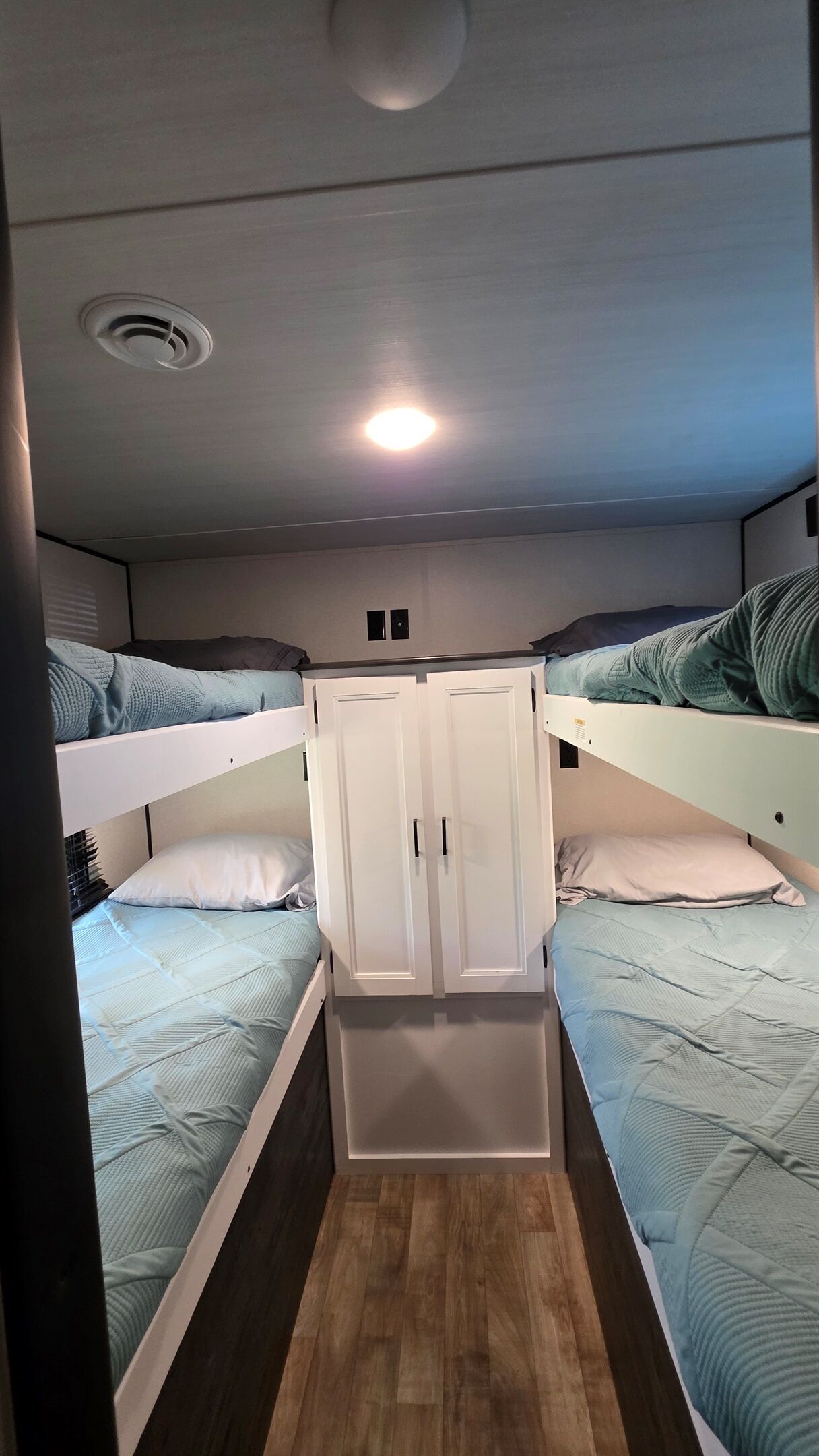Une chambre avec un lit superposé, une armoire et un luminaire au plafond.