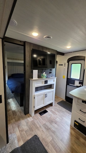 Interior compacto de una autocaravana con cama, un mueble blanco para entretenimiento y una ventana pequeña.