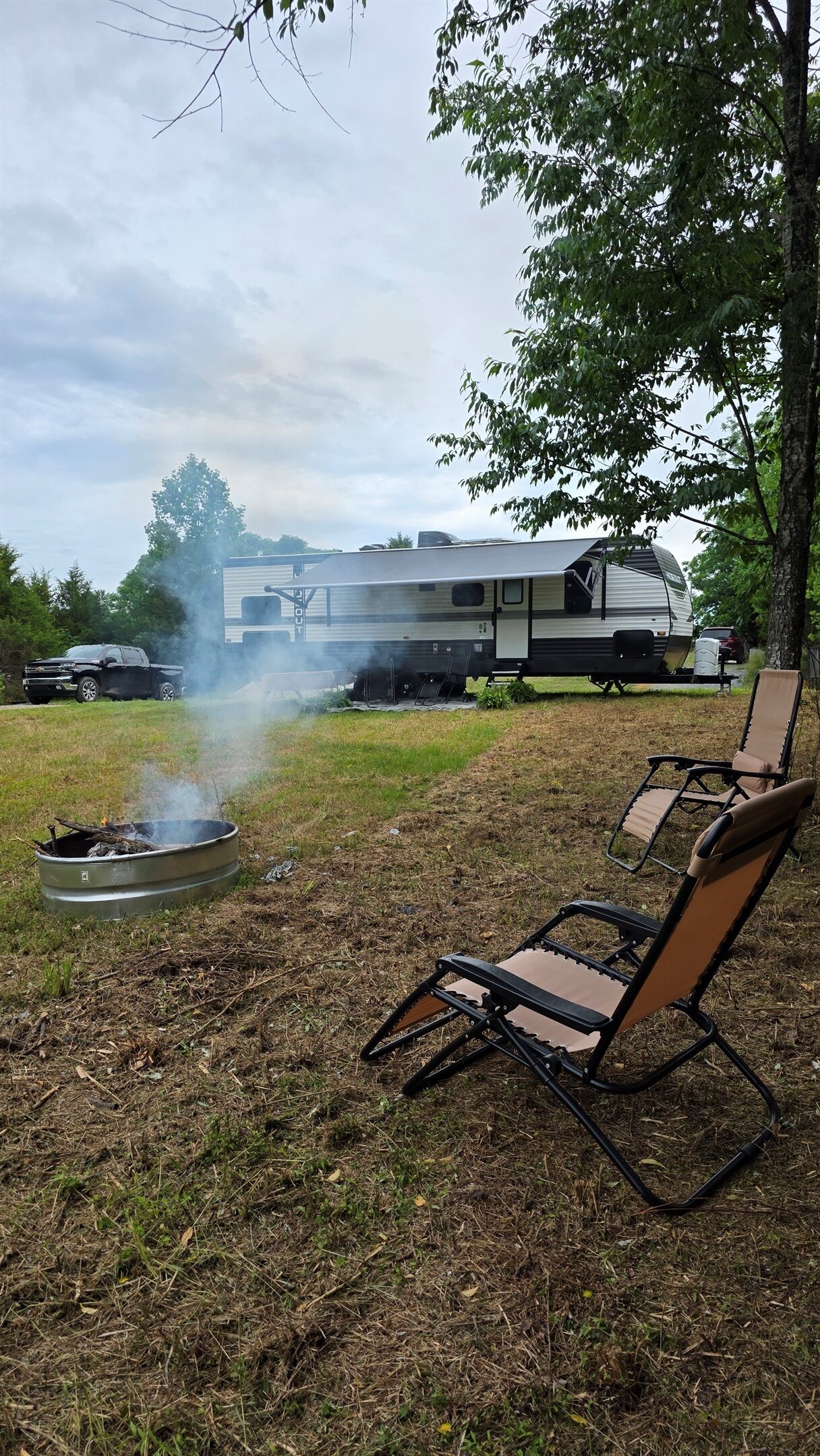 A campsite with a fire pit, a camper, and a lawn chair.