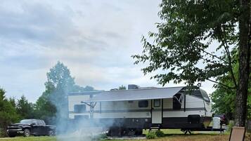 A campsite with a fire pit, a camper, and a lawn chair.