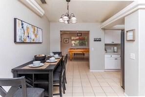 A dining area with a table set for four, a pool table, and a kitchen with white cabinets. - Highlander Retreat - Pool, Pool Table, Comfort (Lake Havasu City)