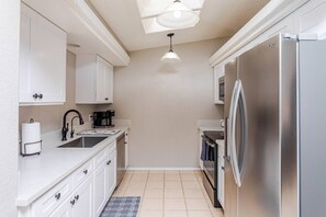 A compact kitchen with white cabinets, a stainless steel refrigerator, a coffee maker, and a tiled floor. - Highlander Retreat - Pool, Pool Table, Comfort (Lake Havasu City)