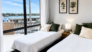 A hotel room with two beds, a nightstand with a lamp, and a view of a marina.