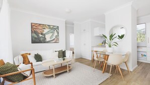 A modern living room with a white sofa, a coffee table, and a dining area with chairs and a small table.