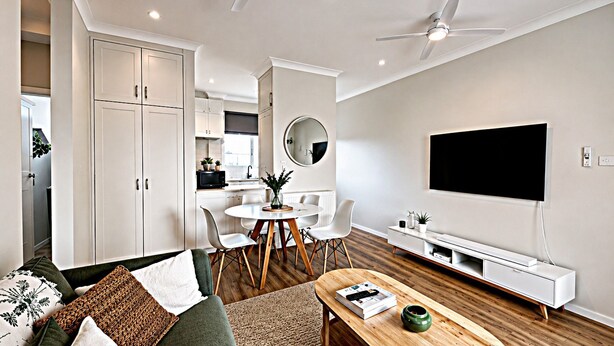 A modern living room with a dining area, a flat-screen TV, and a ceiling fan.