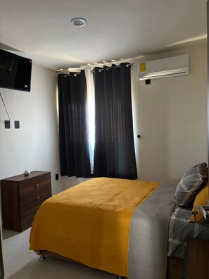 A bedroom with a bed, a dresser, a flat-screen TV mounted on the wall, and an air conditioning unit. - FURNISHED APARTMENT FOR UP TO 6 PEOPLE, BLOSSOM GRAND PARK SUBDIVISION (Puerto Vallarta)