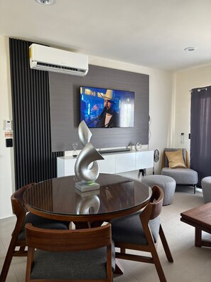 A modern living room with a round dining table, chairs, a mounted TV, and a decorative metal sculpture. - FURNISHED APARTMENT FOR UP TO 6 PEOPLE, BLOSSOM GRAND PARK SUBDIVISION (Puerto Vallarta)
