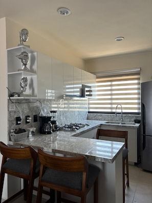 A modern kitchen with granite countertops, a gas stove, a coffee maker, and a refrigerator. - FURNISHED APARTMENT FOR UP TO 6 PEOPLE, BLOSSOM GRAND PARK SUBDIVISION (Puerto Vallarta)
