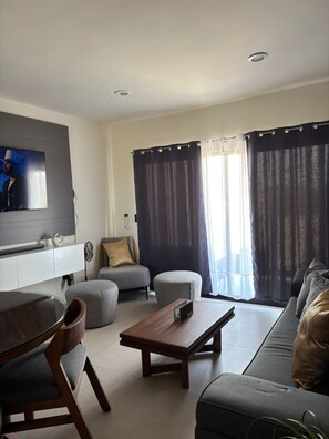 A modern living room with a flat-screen TV, a sofa, a coffee table, and a dining area. - FURNISHED APARTMENT FOR UP TO 6 PEOPLE, BLOSSOM GRAND PARK SUBDIVISION (Puerto Vallarta)
