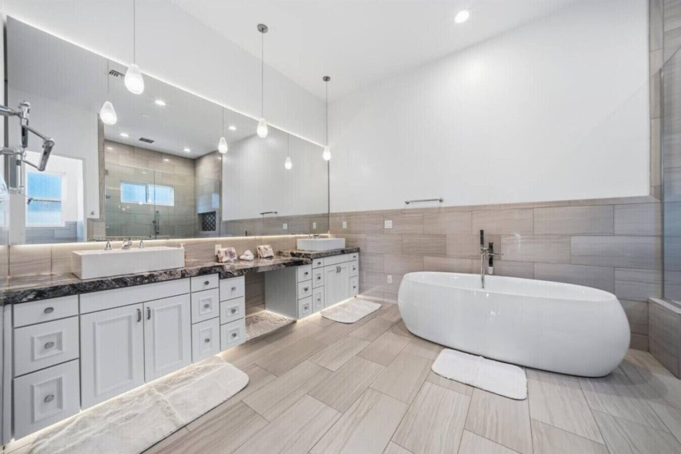 A modern bathroom with a large freestanding bathtub, a double vanity with a mirror, and a light wood floor.