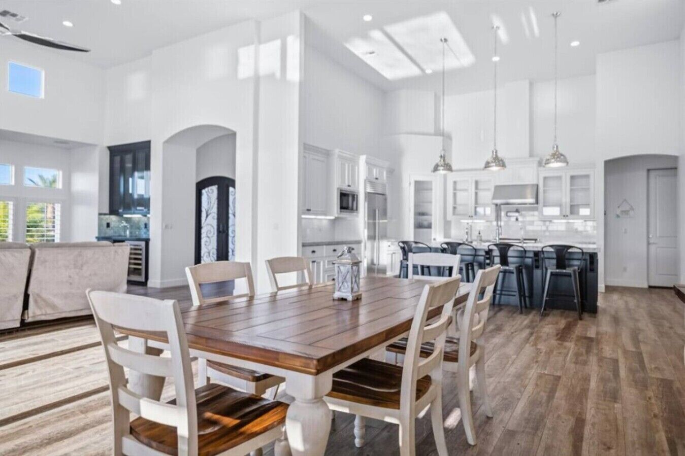 Een ruime keuken met witte kasten, een houten eettafel en een groot eiland met barstoelen.