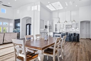 A spacious kitchen with white cabinetry, a wooden dining table, and a large island with bar stools. - Luxury Cardinal Retreat - Pool, Spa, BBQ, Garage (Lake Havasu City)