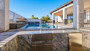 Ein Pool mit einer Steindecke, einem integrierten Grill und einer überdachten Terrasse.