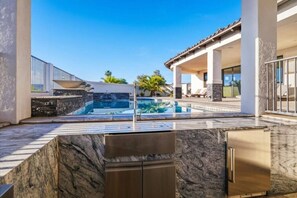A swimming pool with a stone deck, a built-in grill, and a covered patio area. - Luxury Cardinal Retreat - Pool, Spa, BBQ, Garage (Lake Havasu City)