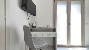 Una habitación moderna con escritorio, silla, televisor y puerta corrediza de vidrio.