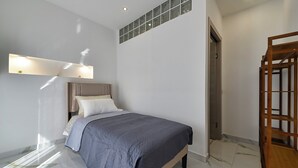 Un dormitorio con cama, mesita de noche, lámpara de pared y puerta.