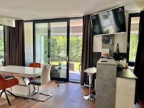 A modern kitchen with a flat-screen TV, a clock, and a small bar area.